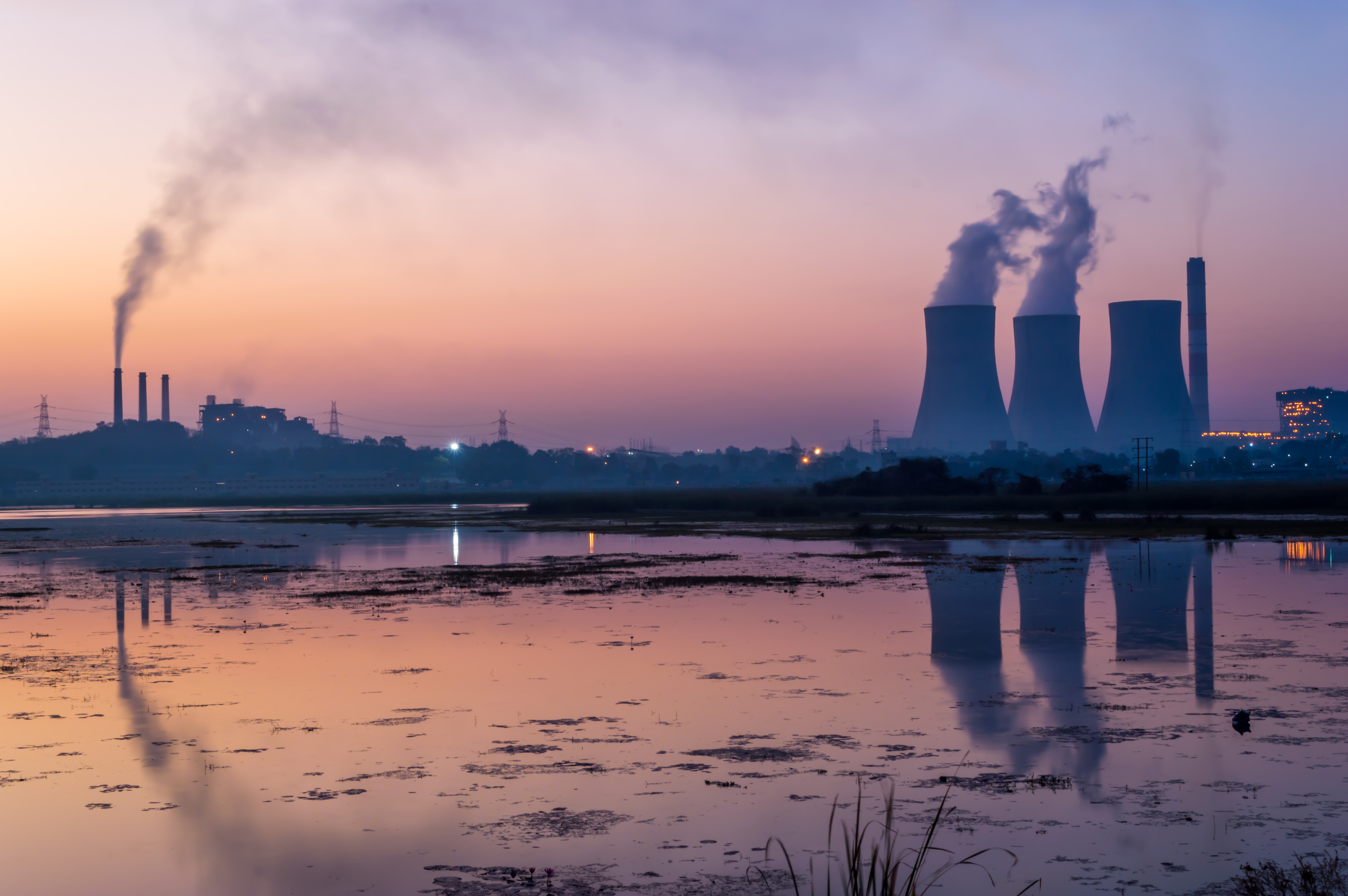 Nuclear power Global South represented by thermal power plant emitting smoke and cooling tower emitting steam. The lake near the electricity generating power plant showing reflections