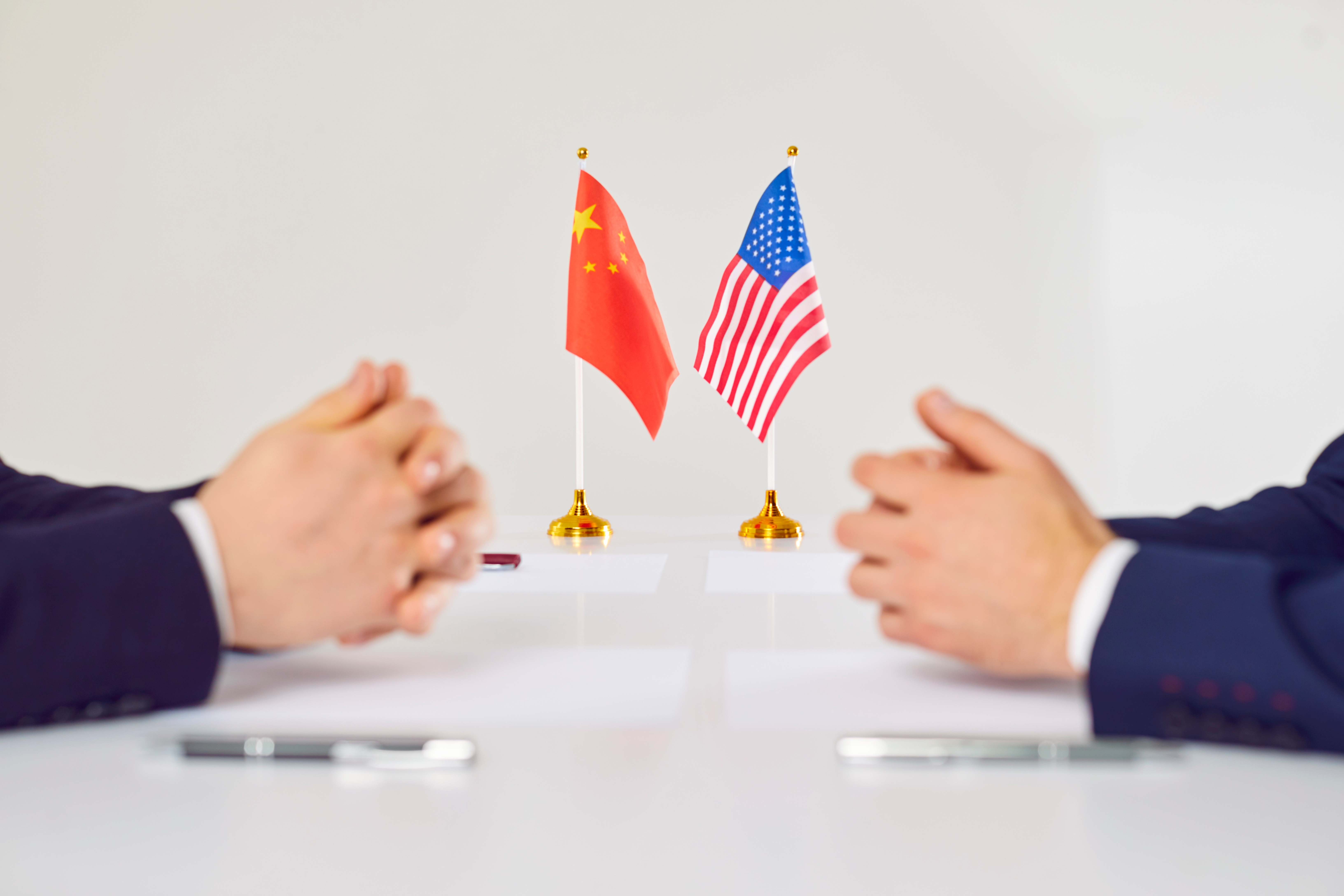 China US tariff reduction deal shown with American and Chinese flags on table as diplomats and business leaders meet face-to-face to discuss bilateral economic cooperation