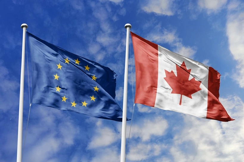 Waving flags of the European Union and Canada together on blue sky background. Official diplomatic relations, partnership and business concept. Source: Shutterstock